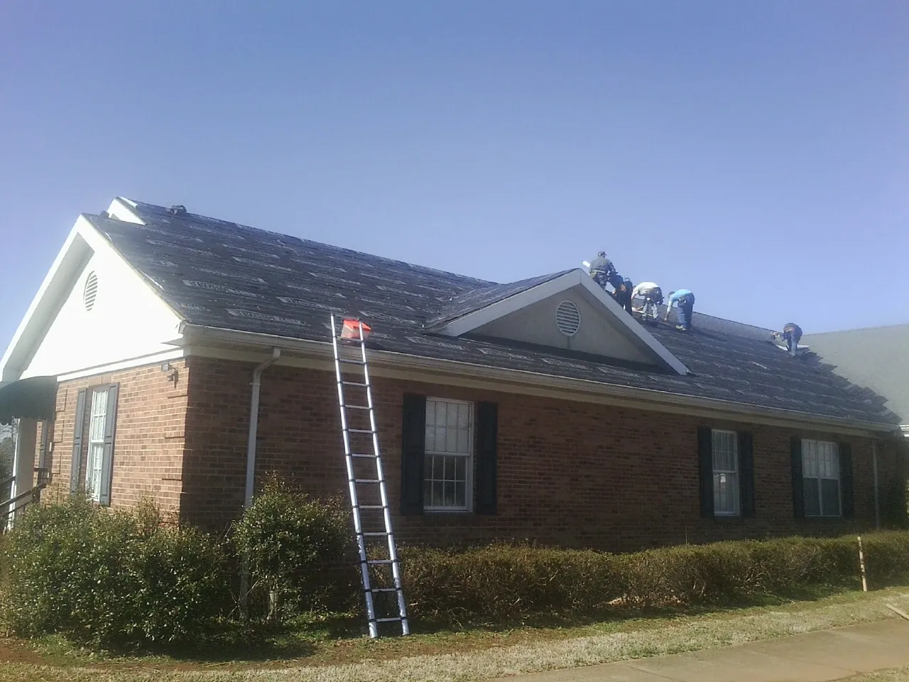 Crew tearing shingles off a brick ranch roof with a ladder set — Emergency Roof Repair work by our crew in Savanna
