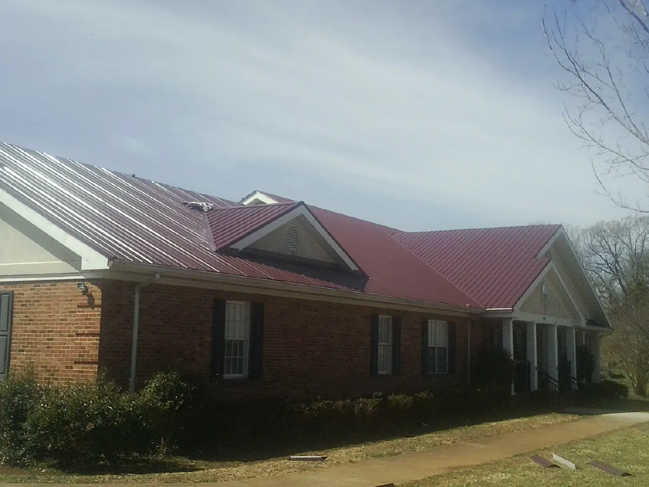 Red metal roof with gabled entries on a long brick building, from a Hail Damage Roof Repair job in Savanna