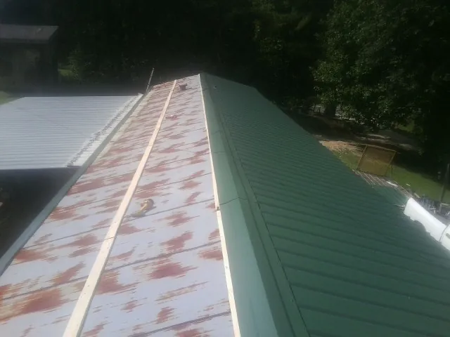 Old rusted panels beside newly installed green metal roofing — Wind Damage Roof Repair by Roofing Brothers in Savanna