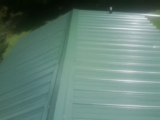New green metal panels meeting at the ridge of a roof — Flat Roof Repair work by our crew in Savanna
