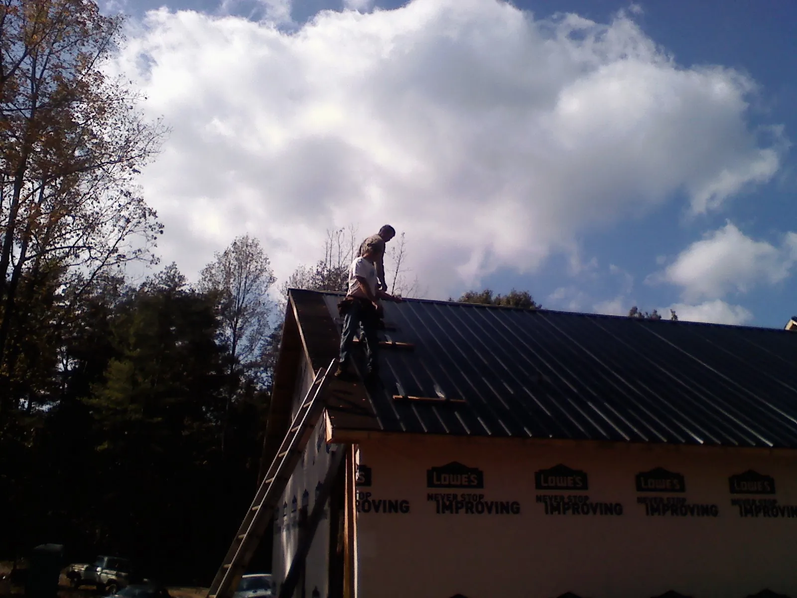 Roofer fastening dark metal panels high against a cloudy sky, from a Roof Inspection job in Savanna