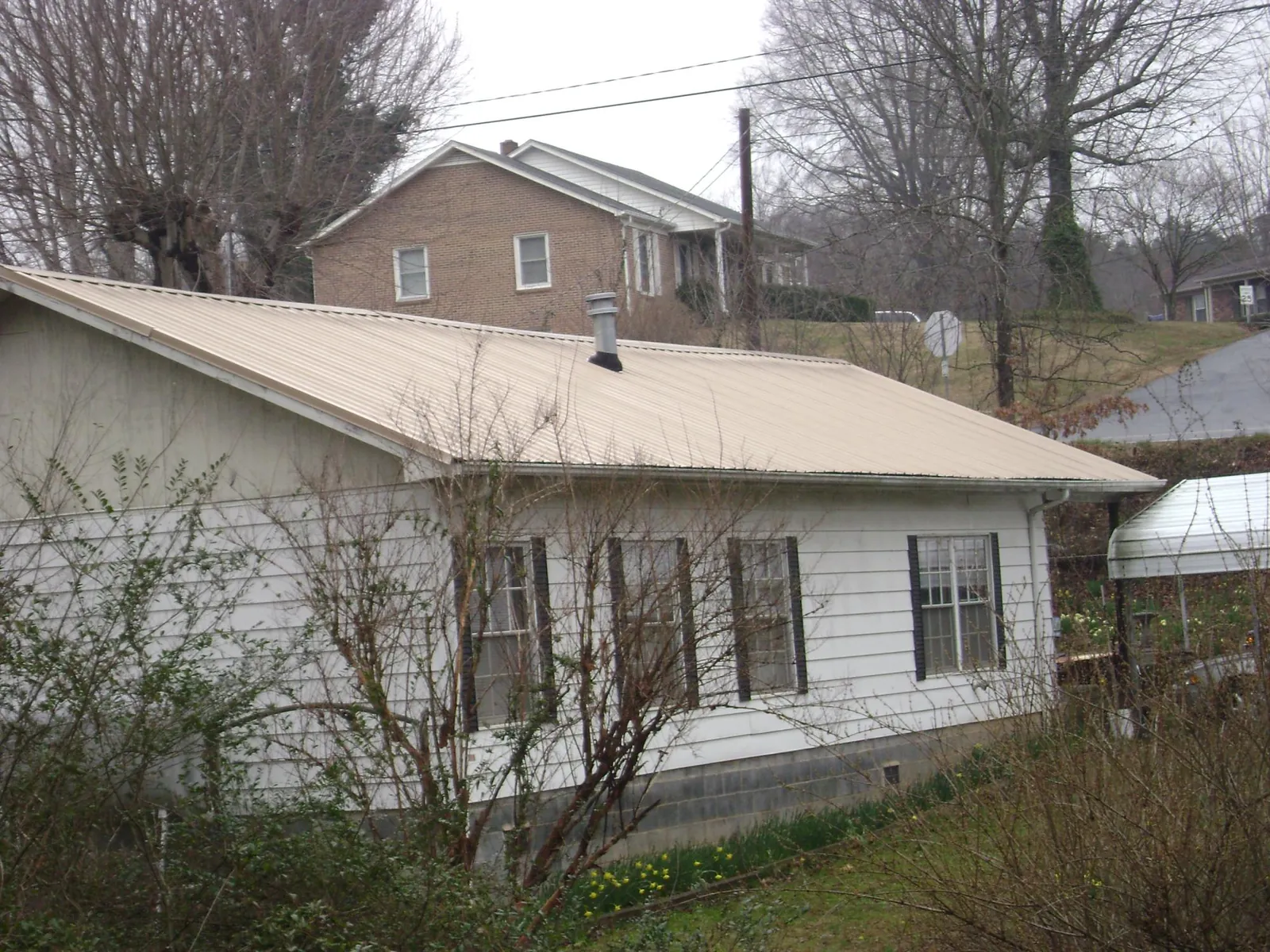 Tan metal roof on a white sided house set into a hillside — Commercial Roofing by Roofing Brothers in Savanna