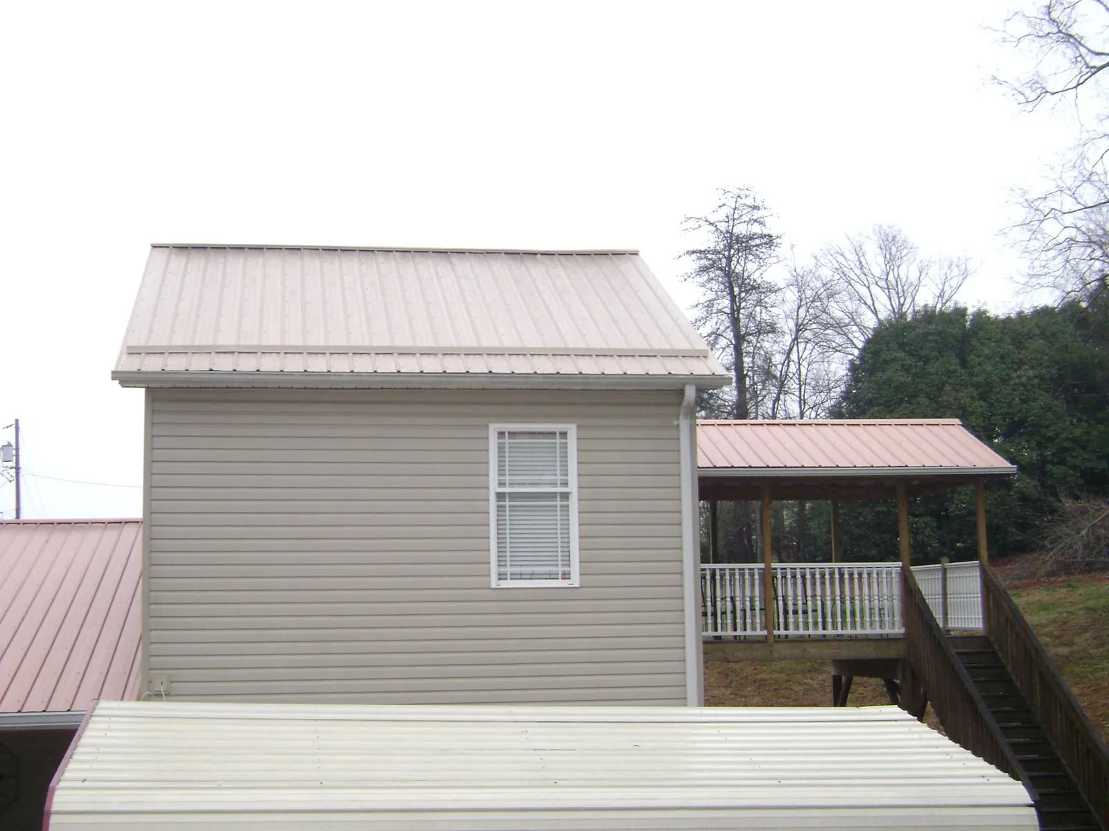 Tan metal roofs on a two story addition and attached porch, from a Roof Replacement job in Savanna